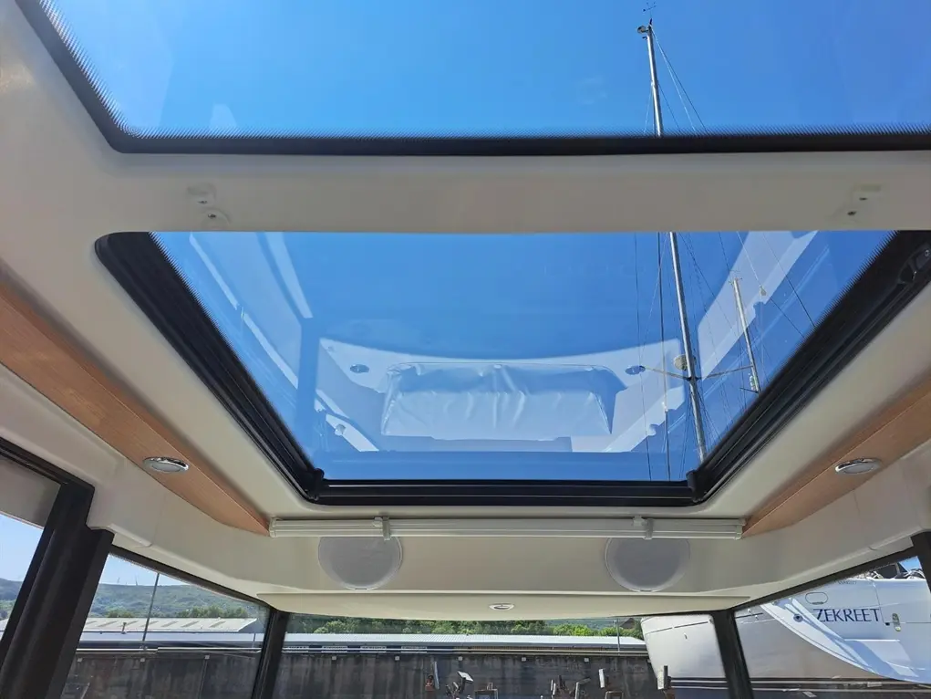 View of a glass skylight on a yacht, showcasing a clear blue sky and the mast of a nearby boat.